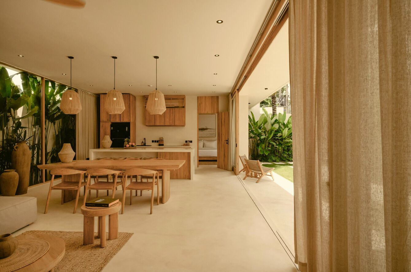 A modern kitchen with wooden cabinets, a dining area with a large table and chairs, and a view of greenery outside.