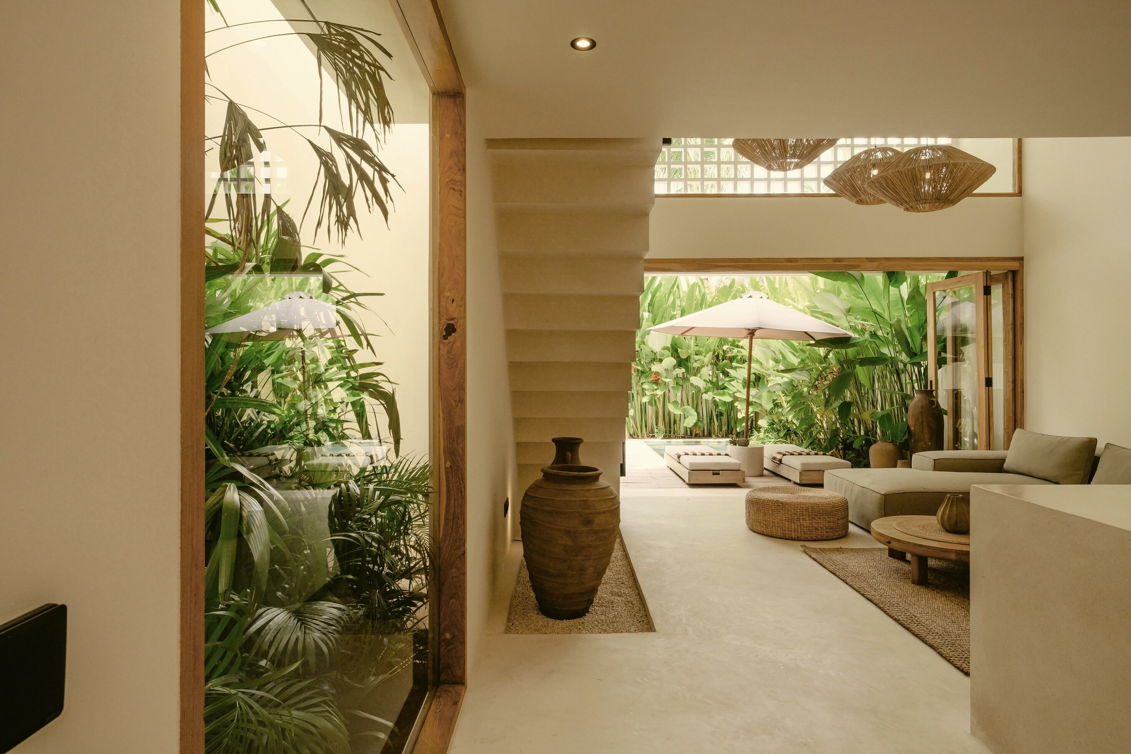 Un intérieur moderne avec un escalier, un coin salon comprenant un canapé et un pouf, et un grand vase.