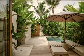 A poolside area with a wooden deck, lounge chairs, a large umbrella, and lush tropical plants. - COZ Bali Boutique Villas (Uluwatu)