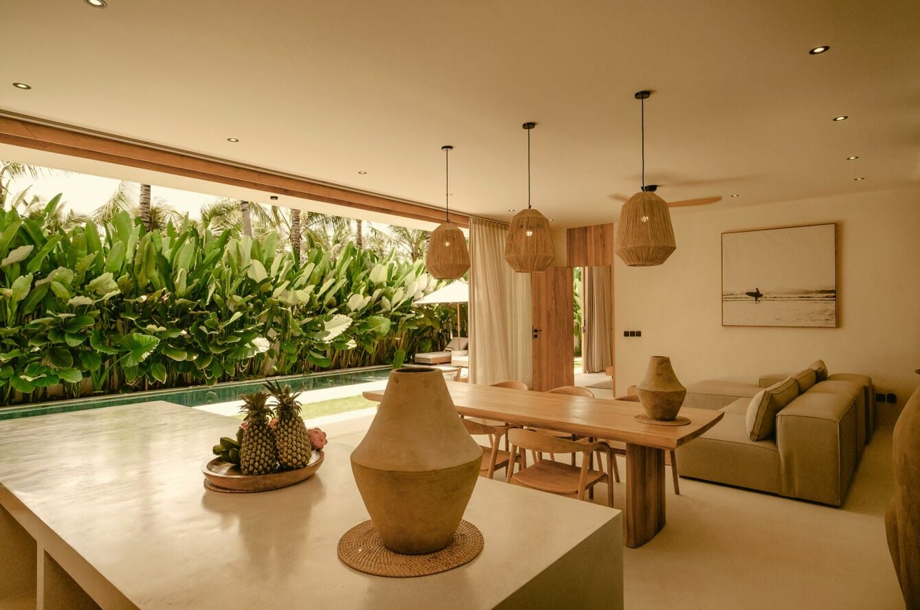 A modern living room with a pool view, wooden furniture, and hanging lights.