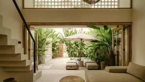 Un intérieur moderne comprenant un escalier, un canapé, un pouf rond et un coin repas avec une table et un parasol.