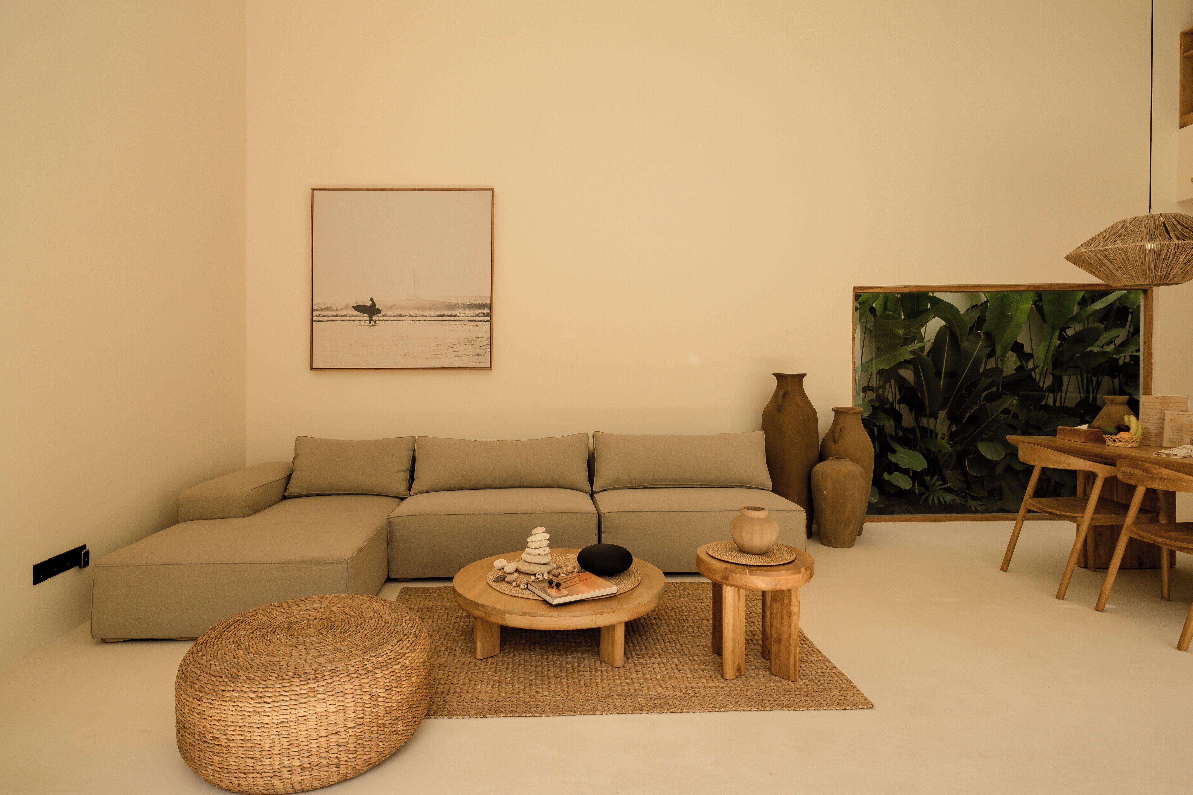 Ein Wohnzimmer mit einer Couch, einem runden Couchtisch mit Dekoration, einem Korbsessel, einem kleinen Holznachttisch und einem Gemälde mit einer Strandansicht.
