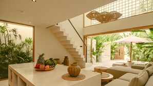 Un salon moderne avec un escalier, un coin repas agrémenté d’un panier de fruits et une vue sur un jardin.