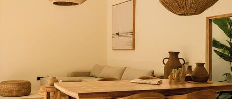 A cozy living room with a wooden dining table, two woven pendant lights, a sofa, and a large framed picture on the wall.