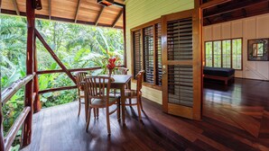 A wooden deck with a table and chairs, a bench, and a view of lush greenery. - La Pina Casita at Bluff Beach Retreat (Isla Colon)