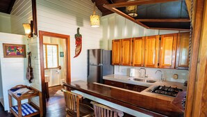 A kitchen with wooden cabinets, a stainless steel refrigerator, a gas stove, and a wooden dining area with chairs. - La Pina Casita at Bluff Beach Retreat (Isla Colon)