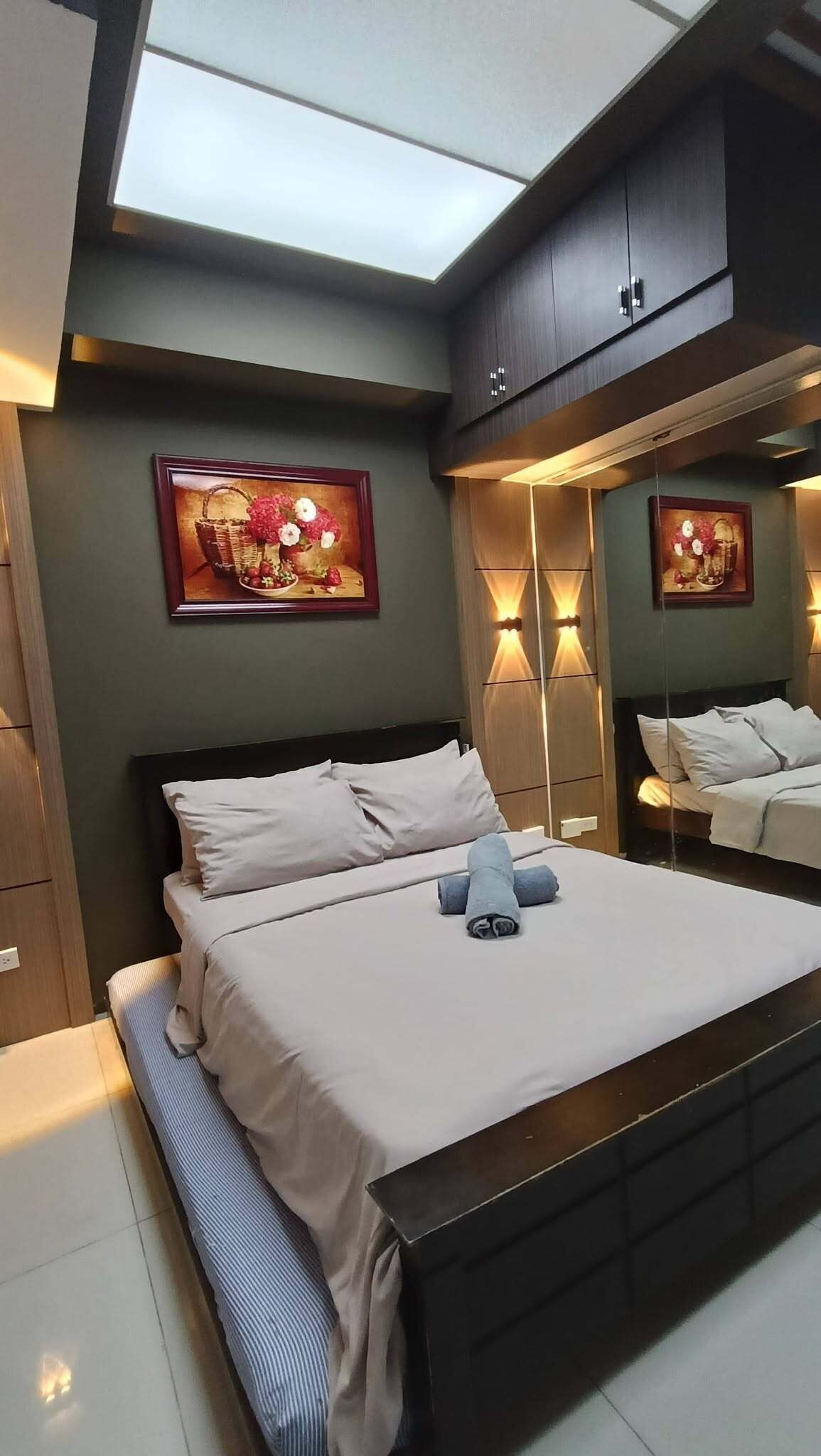 A modern bedroom with a skylight, a large bed, two wall-mounted lamps, and two framed artworks.