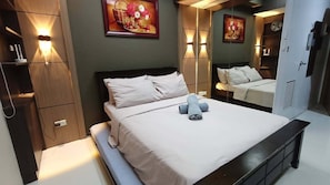 A neatly made bed with pillows and a rolled towel, a bedside table, and a wall-mounted light fixture. - Grand Riviera Suites Manila Condo Infront of us Embassy (Manila)