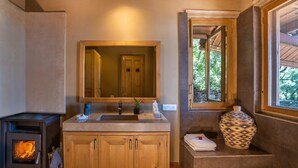 A bathroom with a wooden cabinet, a sink, a mirror, a window, and a fireplace. - Mary Budden Estate Binsar (Kaligari)