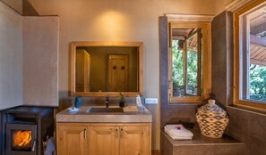A bathroom with a wooden cabinet, a sink, a mirror, a window, and a fireplace. - Mary Budden Estate Binsar (Kaligari)