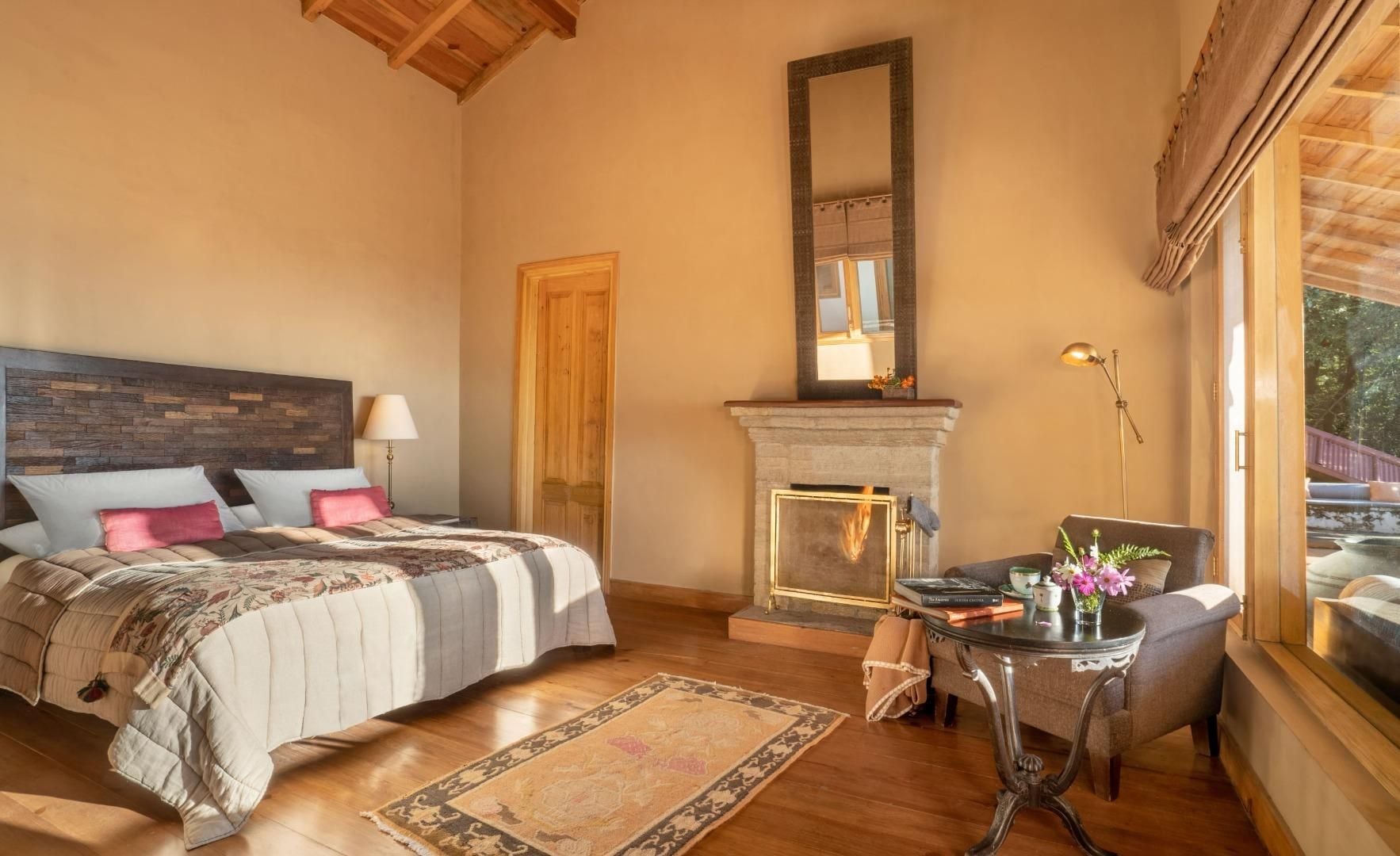 Een slaapkamer met een bed, een open haard, een tafel met een vaas en een raam met uitzicht.