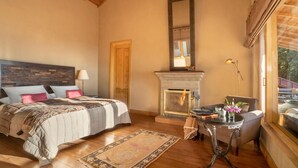 A bedroom with a bed, a fireplace, a table with a vase, and a window with a view. - Mary Budden Estate Binsar (Kaligari)