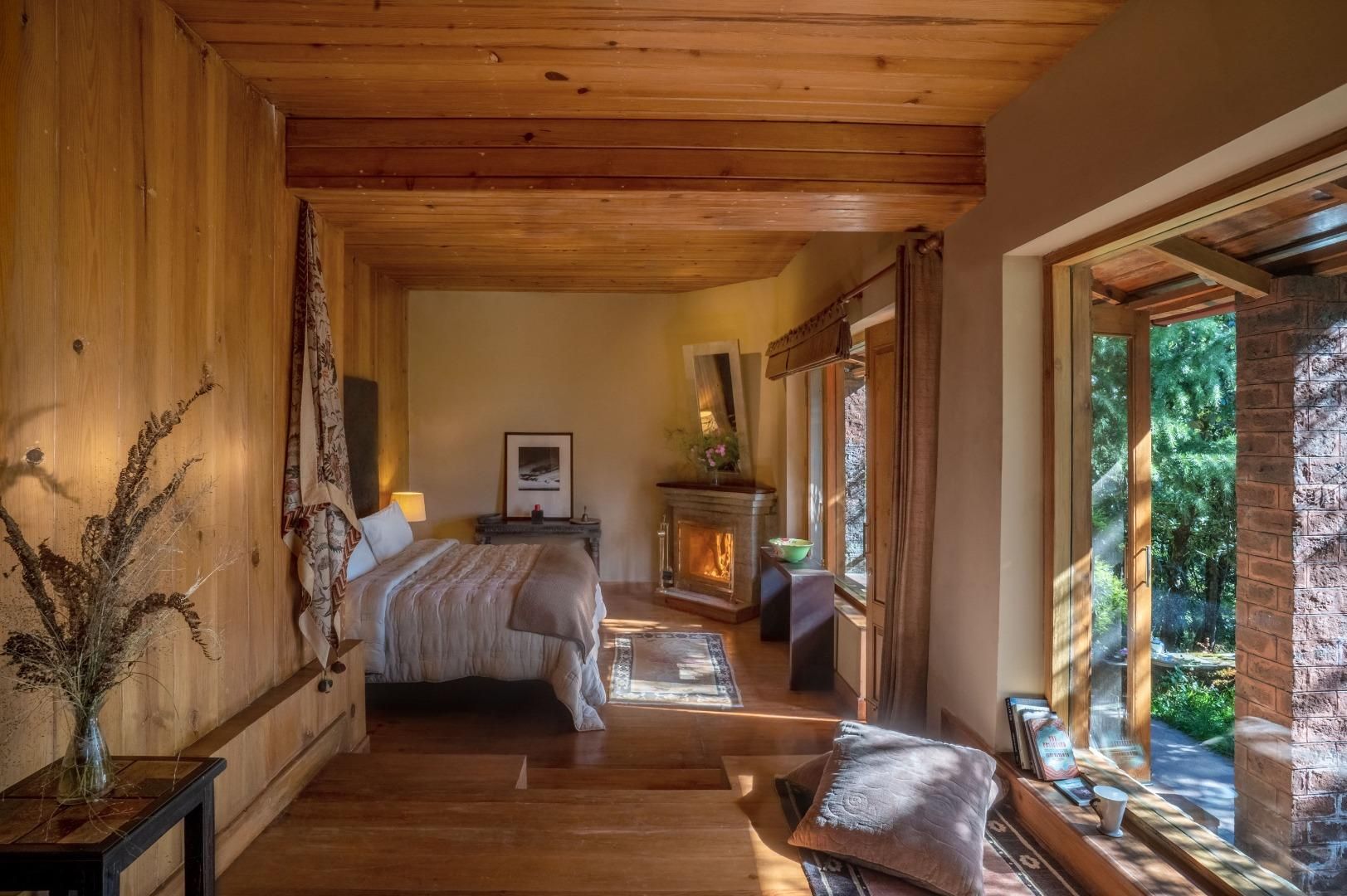 Een gezellig slaapkamer met een houten plafond, een bed, een open haard en een groot raam met uitzicht op groen.