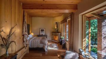 Een gezellig slaapkamer met een houten plafond, een bed, een open haard en een groot raam met uitzicht op groen.