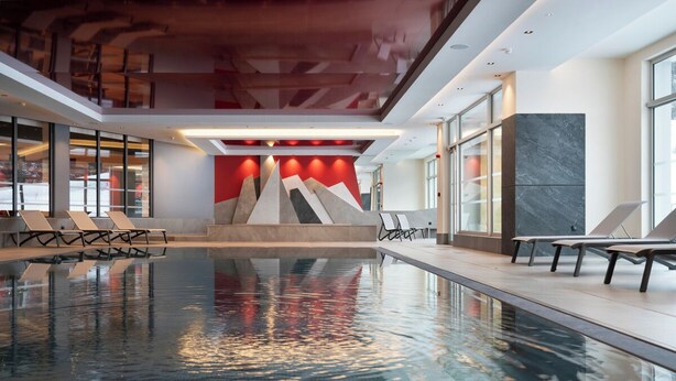 An indoor swimming pool with a modern design, including a geometric wall art installation and lounge chairs along the poolside. - MGM Hôtels et Résidences - Hotel Alhena (Magland)