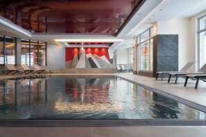 An indoor swimming pool with a modern design, including a geometric wall art installation and lounge chairs along the poolside. - MGM Hôtels et Résidences - Hotel Alhena (Magland)