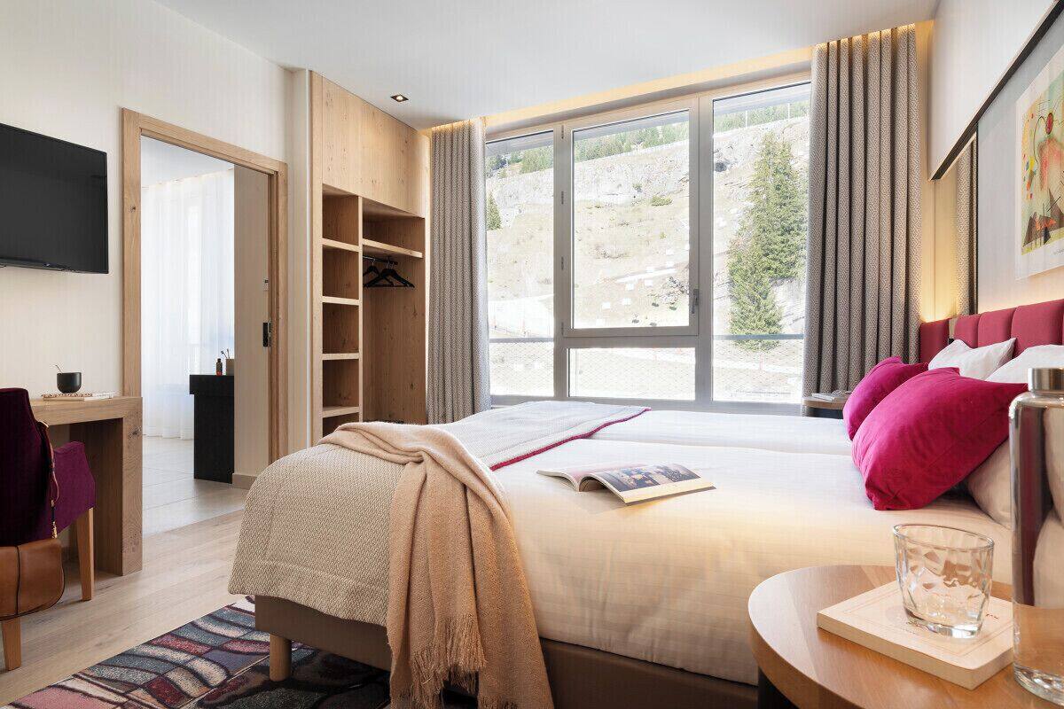 Una habitación de hotel moderna con una cama grande, un escritorio con silla, televisión y vistas al exterior.