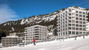 A modern hotel with multiple floors and balconies, set against a backdrop of snow-covered mountains and clear skies. - MGM Hôtels et Résidences - Hotel Alhena (Magland)