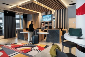 Eine moderne Hotelhalle mit einer Rezeption, einem an einer Holzvertäfelung befestigten Fernseher und einem gemusterten Teppich.