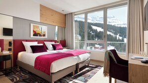 Quarto de hotel moderno com uma cama grande, uma escrivaninha e vista para montanhas nevadas.