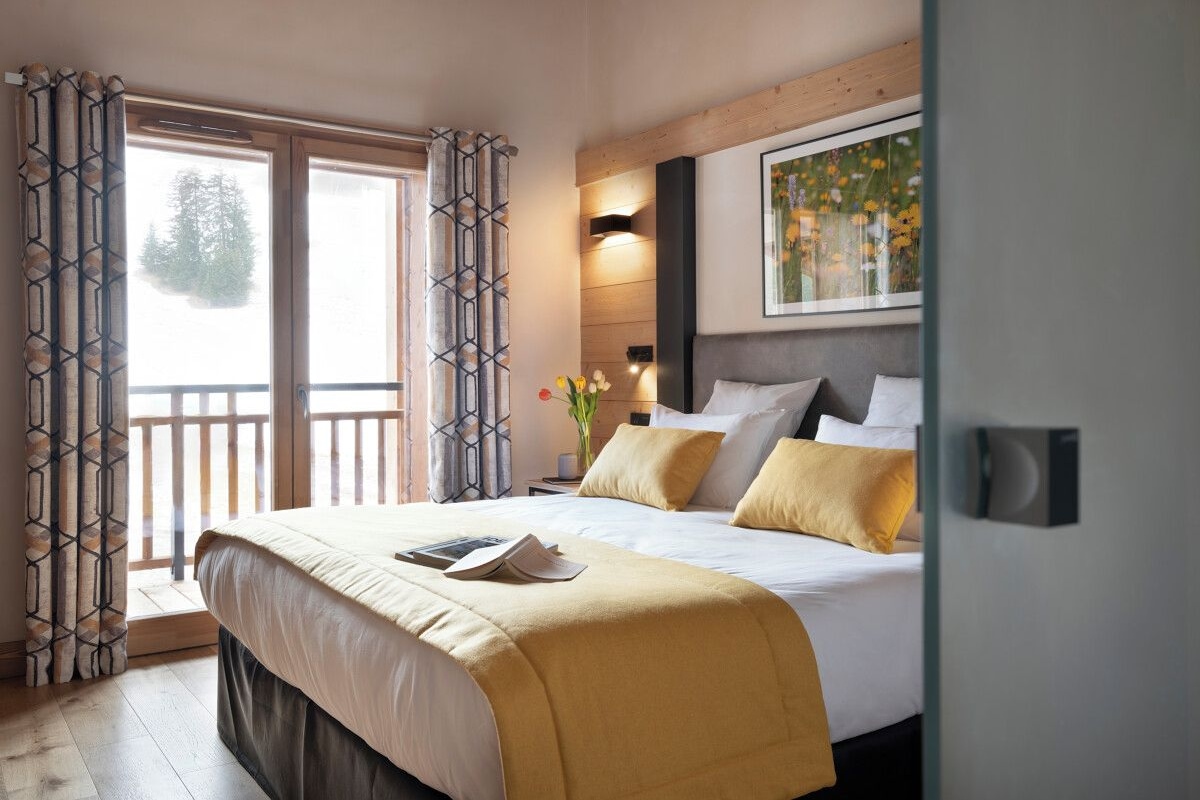 A bedroom with a large bed, a nightstand, a window with curtains, and a painting on the wall.