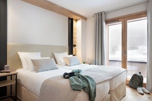 Una habitación de hotel moderna con una cama grande, una mesita de noche y vistas al exterior a través de un amplio ventanal.