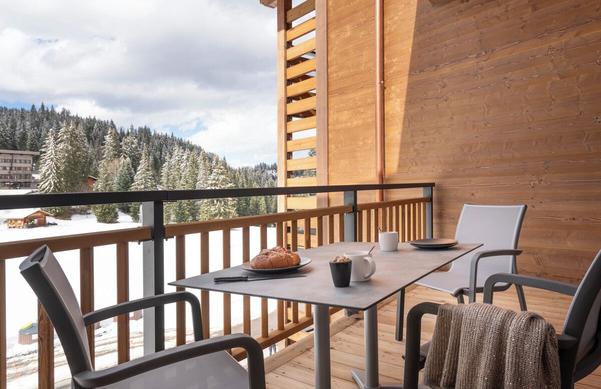Una terraza de madera con una mesa y sillas, con vista a un paisaje nevado con árboles y edificios.
