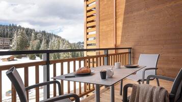 Una terraza de madera con una mesa y sillas, con vista a un paisaje nevado con árboles y edificios.