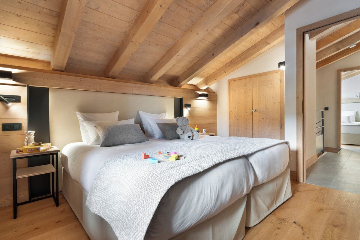 Une chambre avec un plafond en bois, un lit avec une literie blanche, une table de chevet et un ours en peluche.