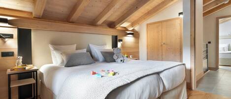 A bedroom with a wooden ceiling, a bed with white bedding, a nightstand, and a teddy bear.