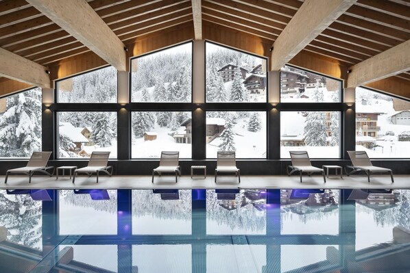 A modern indoor swimming pool with large windows offering views of a snowy mountain landscape. - MGM Hôtels et Résidences - Hameau De L'ours (Manigod)