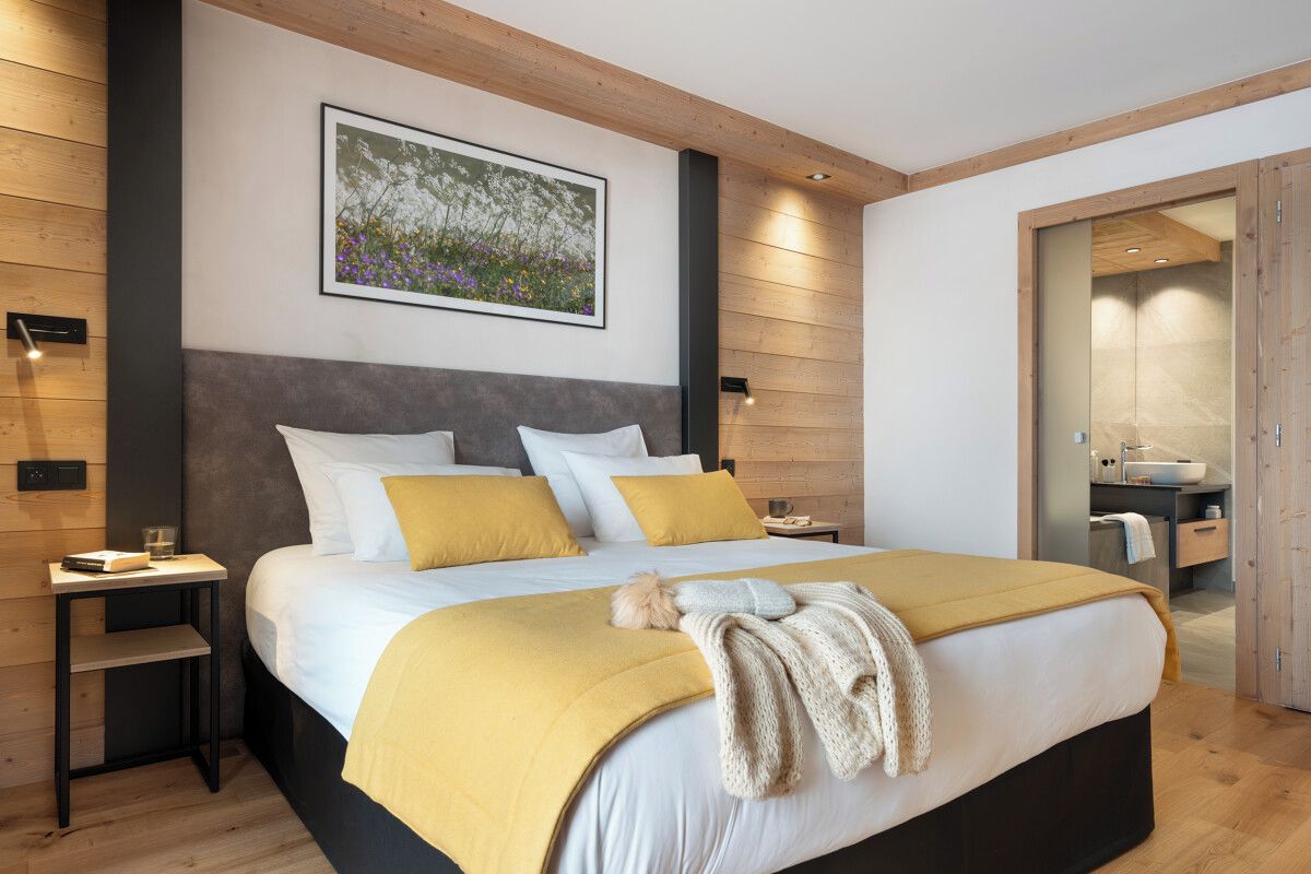 A modern bedroom with a large bed, wooden headboard, and a nightstand.