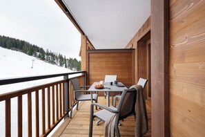 A wooden deck with a table and chairs, overlooking a snowy landscape. - MGM Hôtels et Résidences - Hameau De L'ours (Manigod)