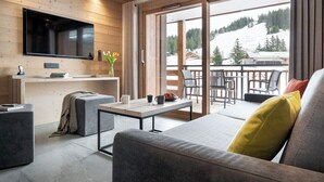 Ein modernes Wohnzimmer mit einem Flachbildfernseher, einer Wand mit Holzvertäfelung, einem Sofa, einem Couchtisch und Blick auf eine verschneite Landschaft durch große Schiebeglastüren.