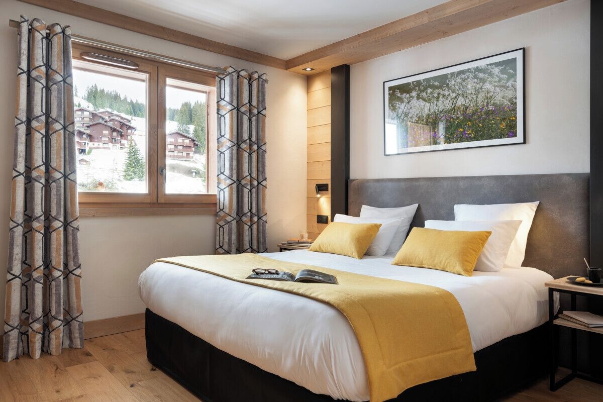A modern hotel room with a large bed, a bedside table, and a window with curtains.
