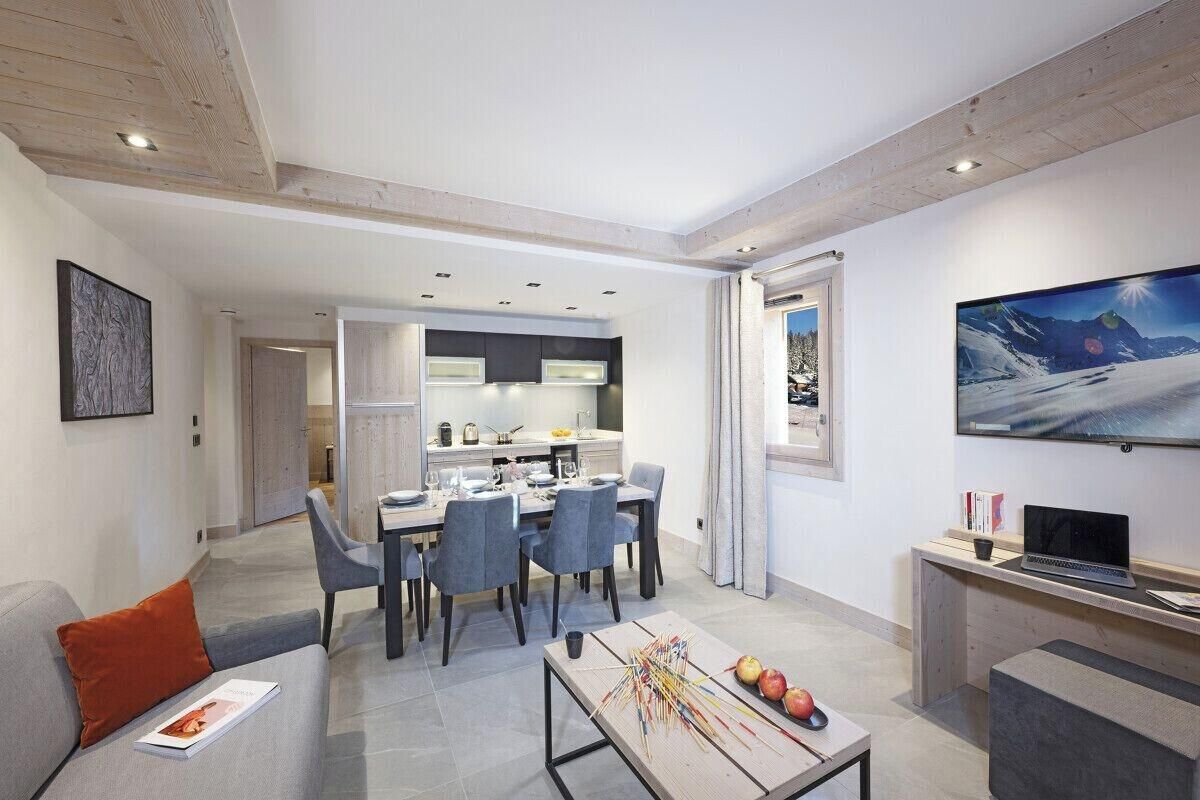 Una sala de estar moderna con comedor, un sofá, una mesa de centro con frutas y un televisor en la pared.