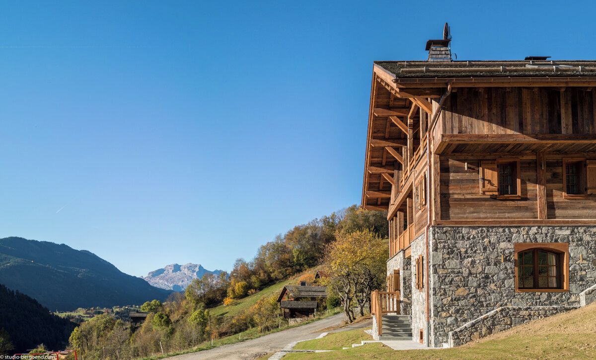 Un chalet en bois aux murs de pierre, doté d’un balcon et offrant une vue sur les collines environnantes.