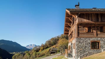 Un chalet en bois aux murs de pierre, doté d’un balcon et offrant une vue sur les collines environnantes.