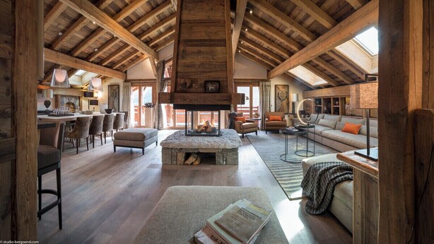 Un loft espacioso con techo alto, vigas de madera a la vista, chimenea de piedra y una zona de estar acogedora con sofá y sillones.