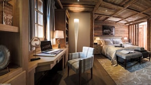 Una habitación acogedora y luminosa, con techo de madera, una cama junto a un gran ventanal, un escritorio con una computadora portátil, una silla y una mesita de noche con una lámpara.
