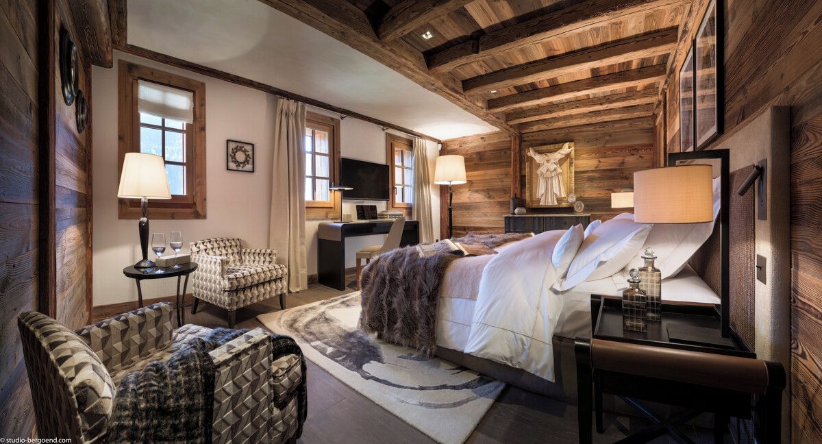 A cozy log cabin-style bedroom with a large bed, a desk, and a chair.