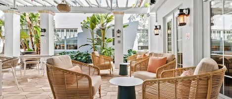 Un espace extérieur aménagé en terrasse, avec des meubles en osier, une table ronde et des plantes en pot.