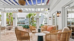 An outdoor patio area with wicker furniture, a round table, and potted plants. - Aloha Fridays Miami Beach (Bal Harbour)