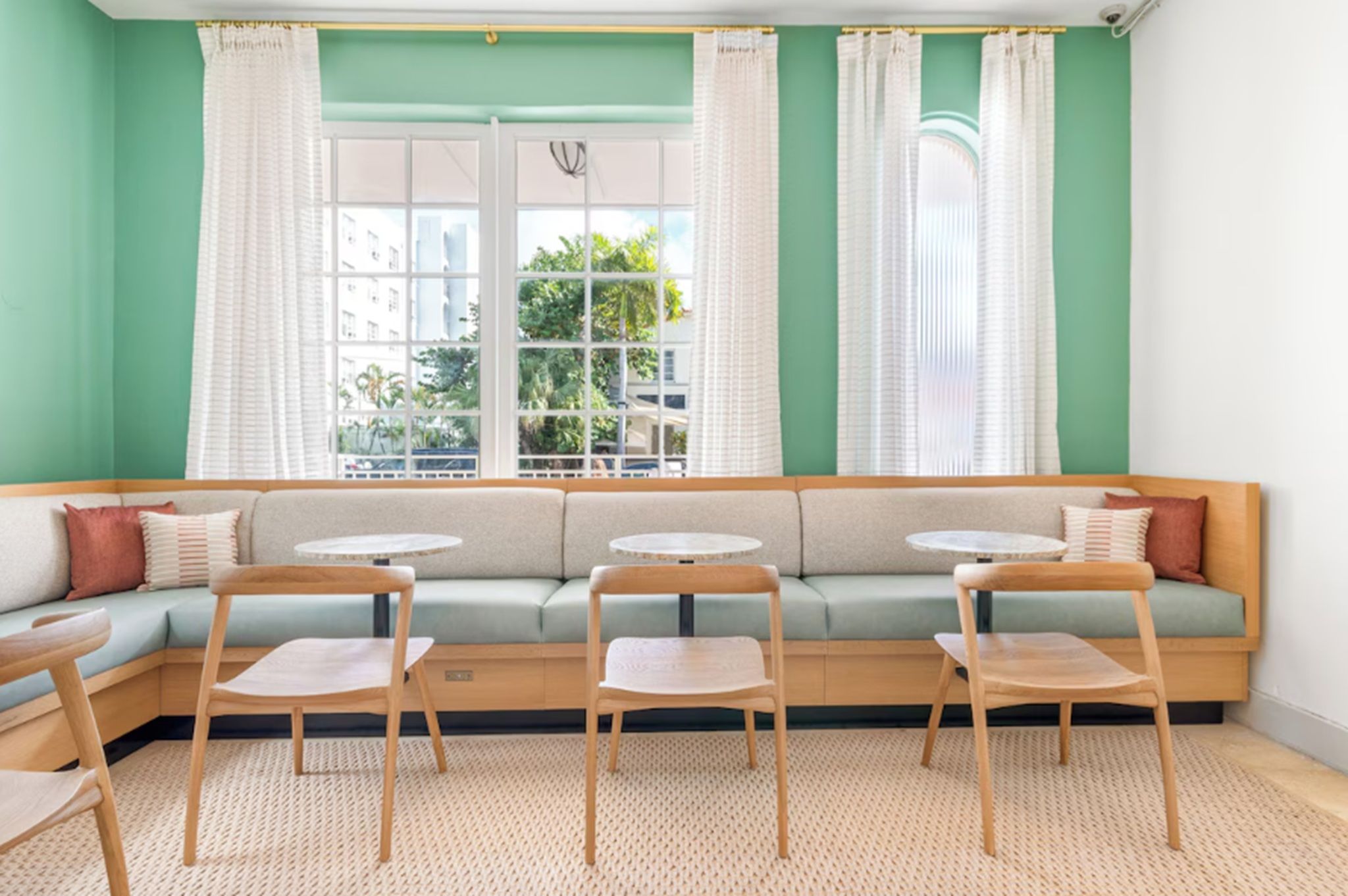 A cozy seating area with a green sofa, two round tables, and wooden chairs.