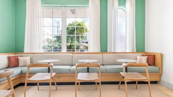 A cozy seating area with a green sofa, two round tables, and wooden chairs.