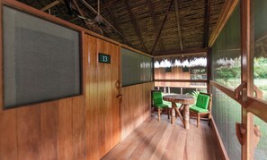 A wooden room with a thatched roof, a number 13 sign, and two green chairs around a wooden table. - Amazon Field Station Byinkaterra (Tambopata)