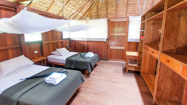 Une chambre avec deux lits, des murs en bois, un bureau en bois et un toit de chaume.