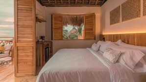 Une chambre avec un lit, des murs en bois, un plafond de chaume, une vue sur des palmiers et un balcon.
