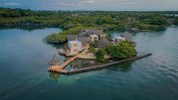 Un complexe hôtelier insulaire comprenant plusieurs bâtiments, un quai et offrant une vue dégagée sur l’eau et la végétation environnantes.