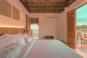 Un dormitorio con cama, cabecera de madera, techo de paja y balcón con vistas al mar.